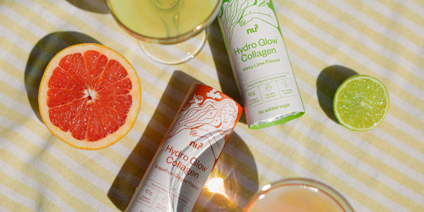 Deux boîtes d'Hydro Glow Collagen sur une nappe rayée jaune avec des verres, un pamplemousse et un citron vert coupés en deux.